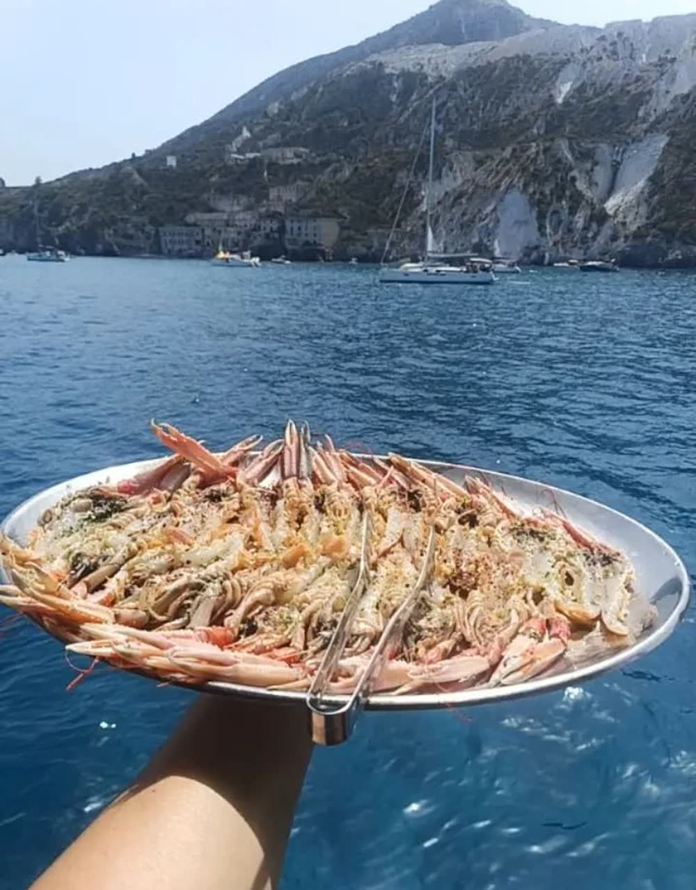 Un vassoio di gamberoni tenuto sopra il mare, davanti alle cave di pomice